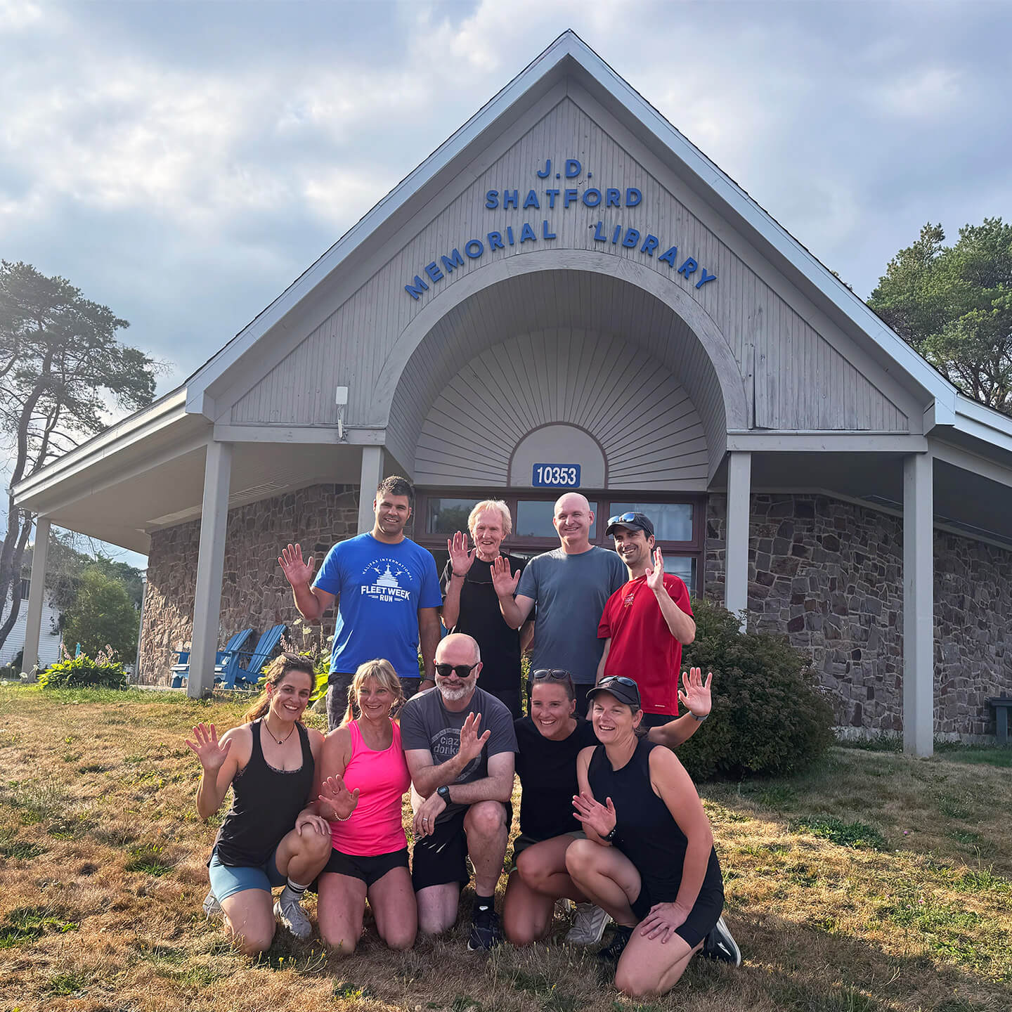 Local Run Club posing outside at the Library entrance, waving and smiling.